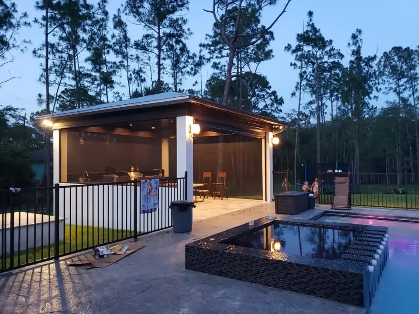 Poolside pavilion with motorized retractable screens at dusk