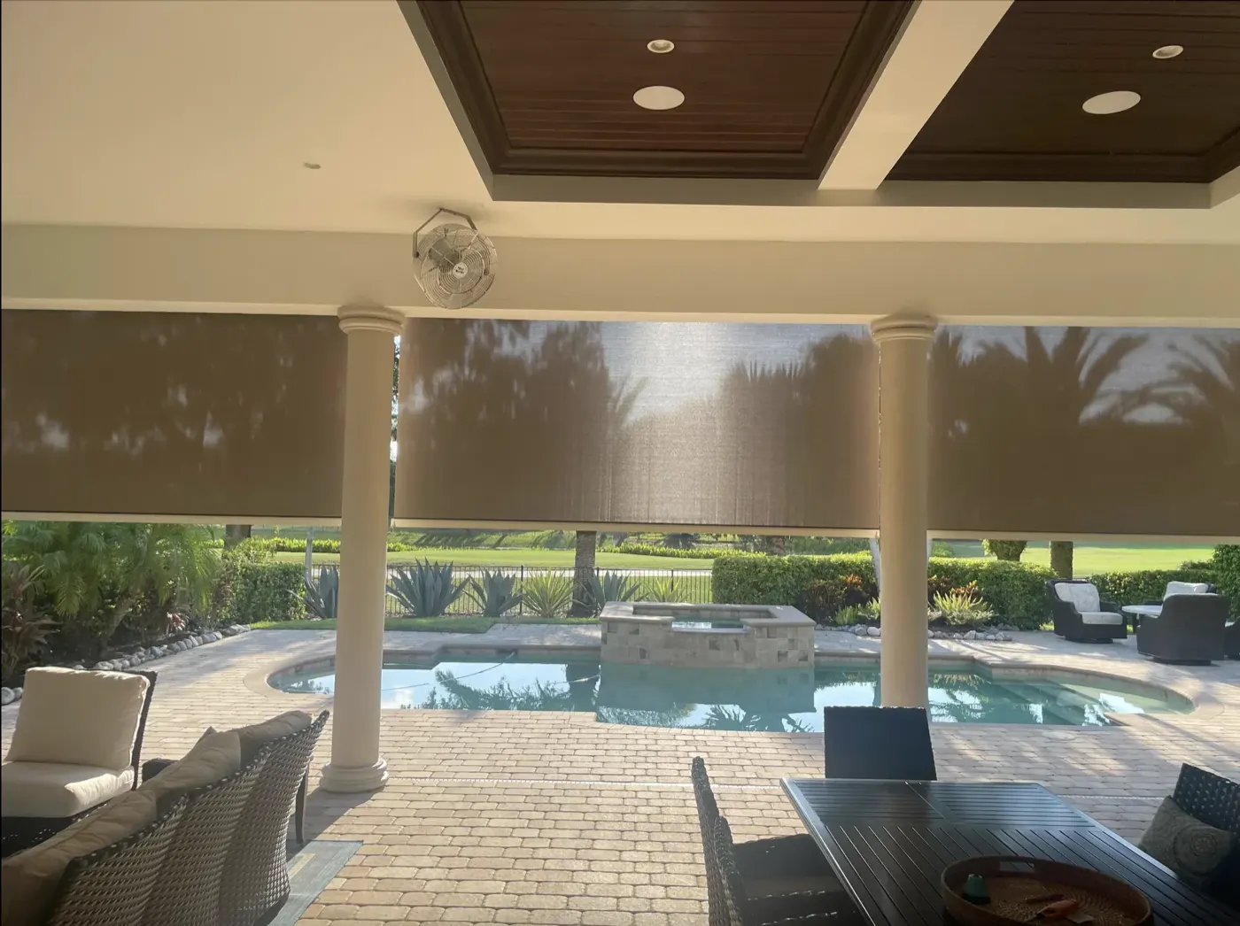 Motorized exterior roller shades on a covered patio overlooking a pool